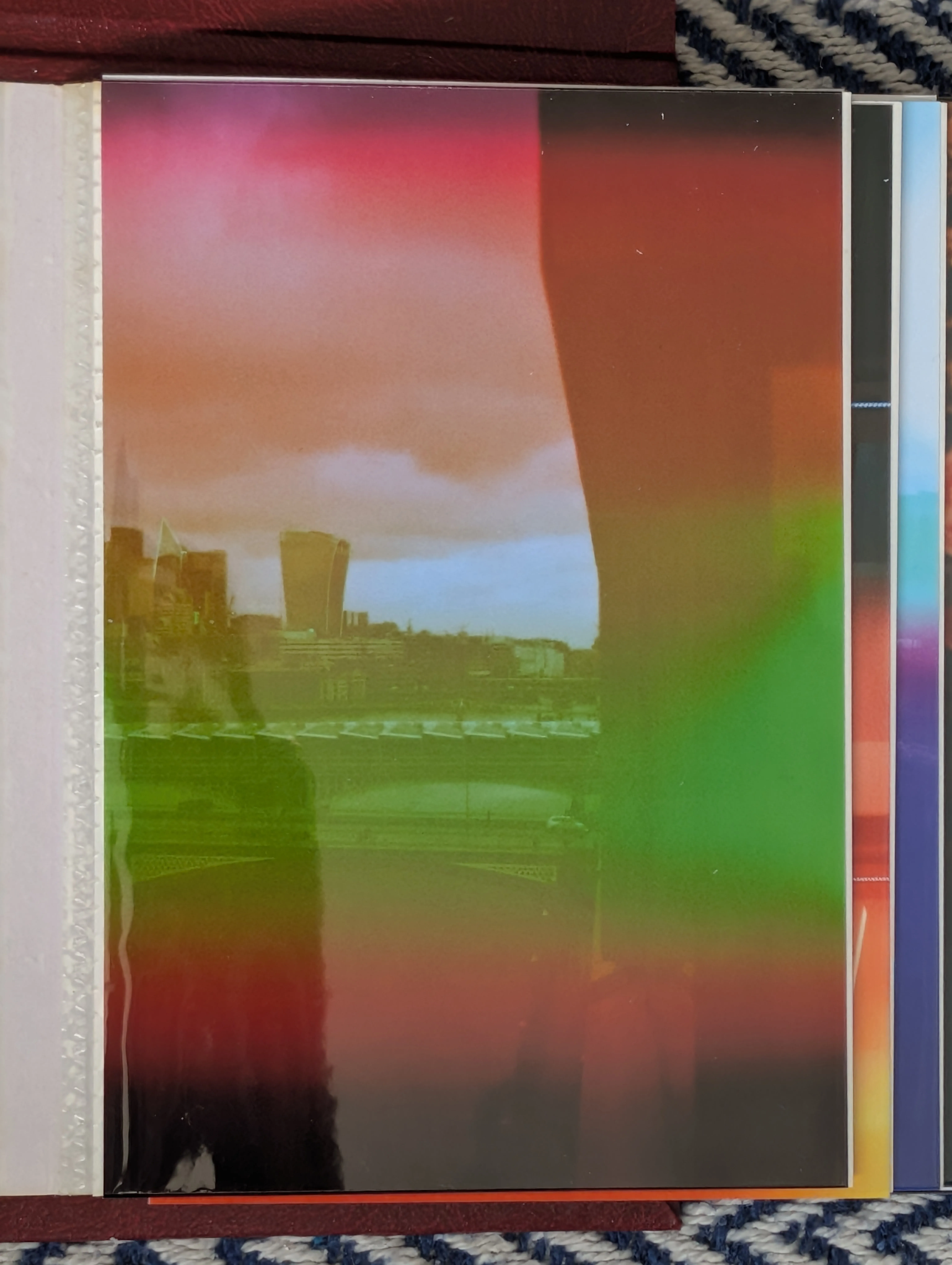 A film print in an album: the London skyline and a Thames bridge under heavy magenta and green light leaks