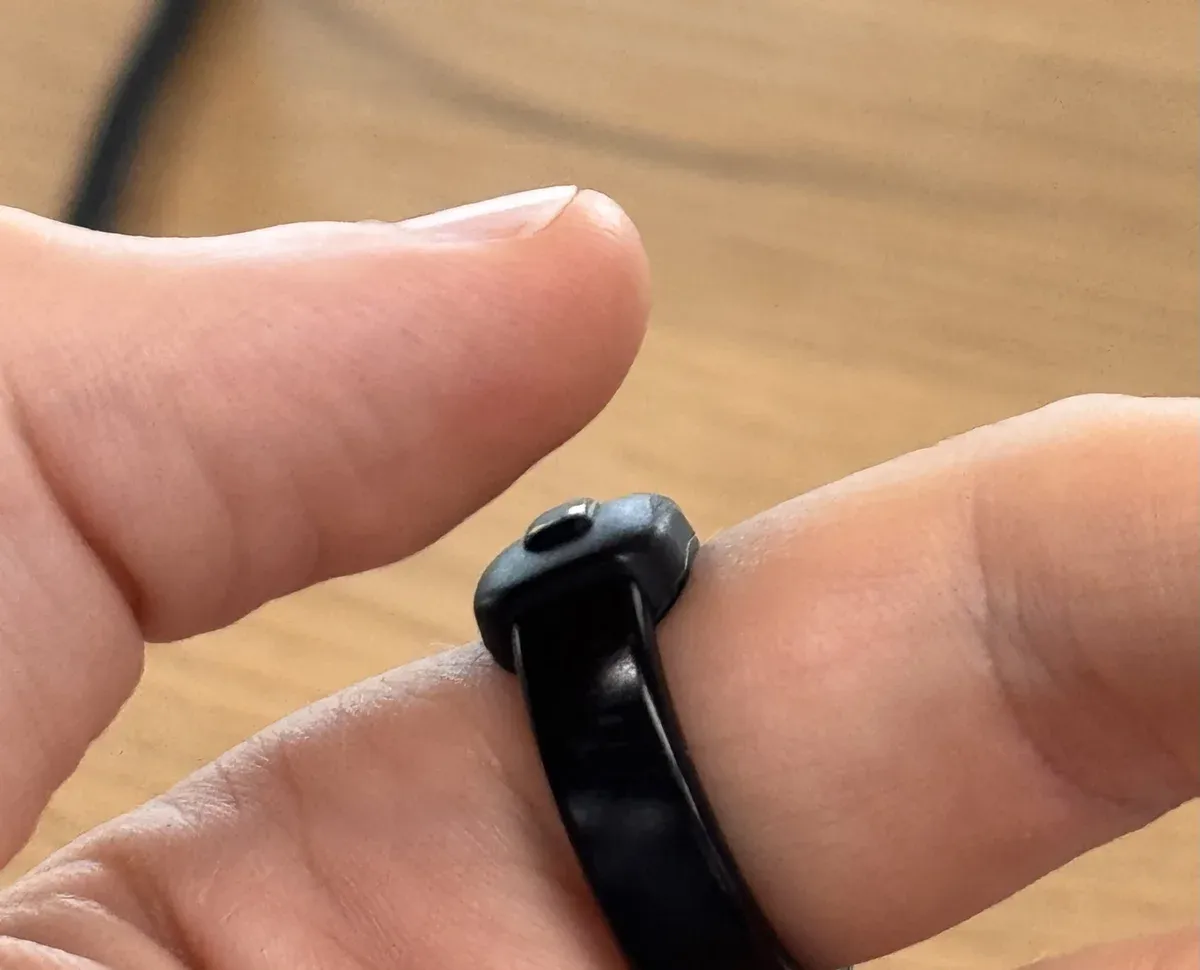 A close-up of a thumb about to click the Index 01 ring worn on another finger